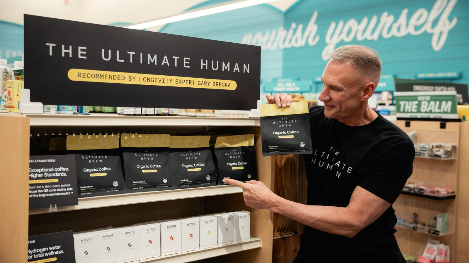 Gary Brecka at The Ultimate Human endcap in Sprouts, pointing to bags of The Ultimate Brew on the top shelf