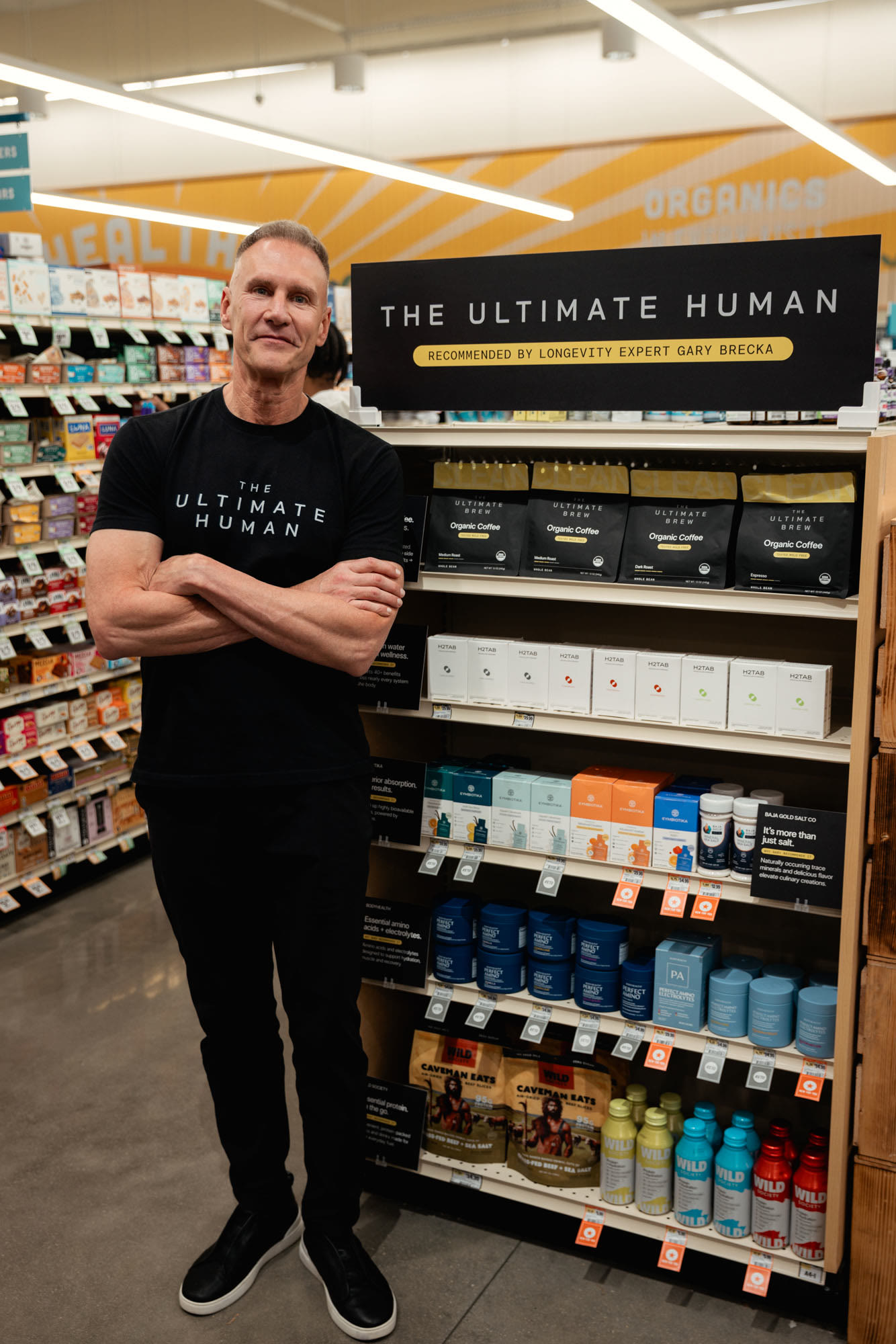 Gary Brecka beside The Ultimate Human endcap in Sprouts, with The Ultimate Brew on the top shelf